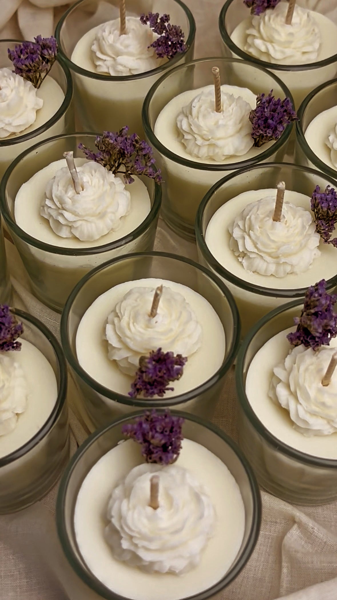 Candle holders with white wax and purple flowers on a neutral background